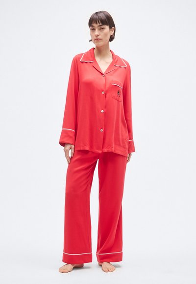 Červený hodvábny pyžamový set s dlhými rukávmi, košeľou na gombíky s vreckom a bielym lemovaním na golieri a manžetách. Voľné široké nohavice.