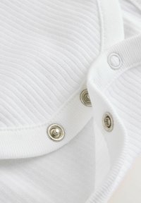 Gros plan d'un tissu blanc côtelé avec des boutons-pression métalliques partiellement fixés sur le bord d'un vêtement.