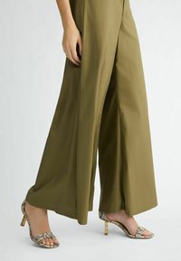 Pantalons à jambes larges oliviers en tissu lisse, associés à des sandales à brides avec un imprimé serpent et des talons rehaussés de doré.