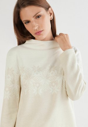 Pull léger en crème avec un col haut, présentant un motif de flocons de neige subtil sur la poitrine et des manches longues. Texture douce et confortable.