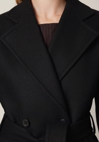 Czarny płaszcz dwurzędowy z szerokimi klapami, wykonany z miękkiej mieszanki wełny, z paskiem do wiązania i gładką fakturą.