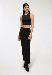 Top corto nero con scollatura alta, abbinato a una gonna lunga nera. Entrambi i capi presentano una texture liscia, progettati per una silhouette aderente.