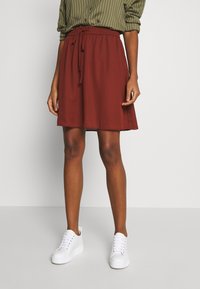 Falda A línea granate con cintura elástica y cordón, combinada con zapatillas blancas. La tela parece suave y ligeramente caída.