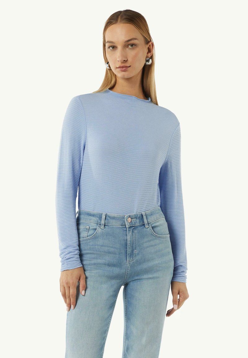 Langärmliges, hellblaues Oberteil mit strukturiertem Stoff, rundem Ausschnitt und tailliertem Schnitt, kombiniert mit hoch sitzenden, hellblauen Jeans.