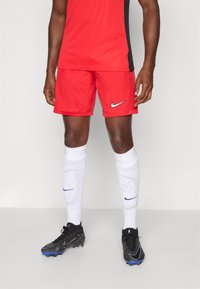Røde sportsshortser med svart akcent, kombinert med hvite sokker med en blå Nike-logo og svarte fotballsko med blå detaljer.