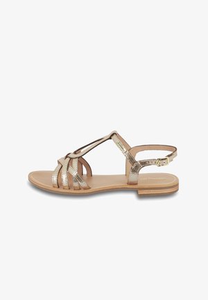 Strappy flat sandals in metallic gold, featuring a T-bar design, ankle buckle, and smooth leather insole with a flat wooden sole.