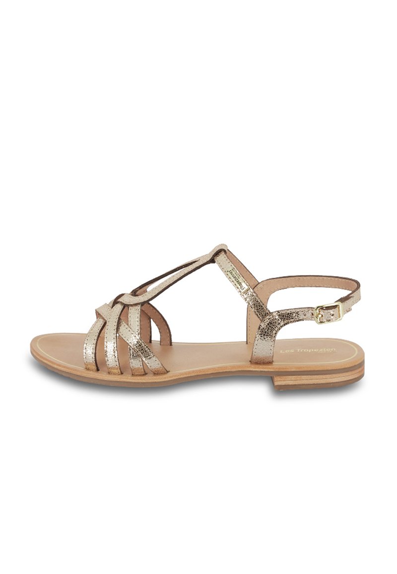 Sandali piatti con cinturini in oro metallico, caratterizzati da un design a T, fibbia alla caviglia e soletta in pelle liscia con suola in legno piatta.