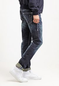 Bleka mörkblå denimjeans med vit sömnad, raka ben och distinkta bakfickor. Kombinationen med vita högre sneakers.