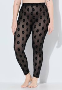 Leggings neri trasparenti con un motivo di teschi ripetuto. Il materiale è leggero e semi-trasparente, con un design aderente.