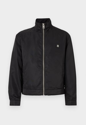 Veste noire à fermeture éclair avec col montant, manches longues, poches latérales et petit logo "HUGO" sur le côté gauche de la poitrine.