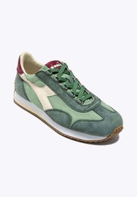 Sneaker verde in suede con accenti verde chiaro e crema. Presenta un design con lacci, materiali texturizzati, suola in gomma e dettagli cuciti.