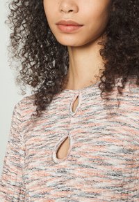 Camisola de malha com um padrão texturizado em creme, laranja e preto. Apresenta recortes ovais e um decote redondo com um acabamento subtil.