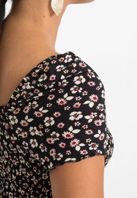 Šaty s květinovým vzorem v černé barvě, s krátkými nafouknutými rukávy, smockovaným živůtkem a růžovými a bílými květinami. Měkká, texturovaná tkanina.