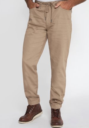 Beige, leichte Hose mit elastischem Bund, Kordelzug und seitlichen Taschen. Schmal zulaufende Beine mit umgeschlagenen Säumen. Kombiniert mit braunen Stiefeln.