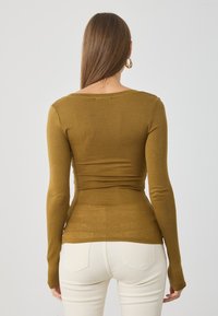 Camisola de manga longa, ajustada, em verde oliva, feita de tecido de malha canelada. Apresenta um decote em forma de barco e uma textura suave, com detalhes mínimos.