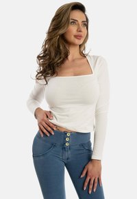 Haut blanc à manches longues avec un décolleté carré associé à un jean taille haute bleu doté de grands boutons dorés et d'un design ajusté.