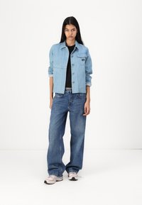 Lys blå denimjakke med skulderepauletter og brystlomme, parret med løstsittende mørkeblå denimjeans og lyse sneakers.