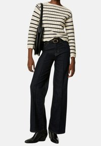 Bluzka w paski w kremowo-czarne, z długim rękawem, ciemne szerokie dżinsy z kontrastowymi szwami, czarny pasek i czarne botki na obcasie. Czarna torebka.