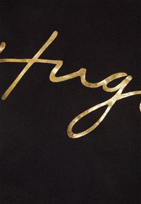 Gros plan sur un texte en cursive dorée brillante sur un tissu noir, mettant en valeur les lettres "fray" avec une texture métallique et une surface lisse.