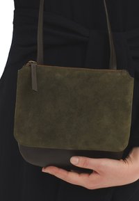 Prekrivena maslinastozelenom antilop kožom i tamnosmeđom kožom, torba preko ramena koju drži osoba u crnoj odjeći.