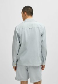 Lyseblå stribet skjorte med lange ærmer, der har en klassisk krave og manschetdetaljer. Bæres med matchende shorts.