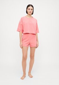 Pink cotton crop top with short sleeves, paired with matching shorts. Both pieces feature a soft texture and a relaxed fit.