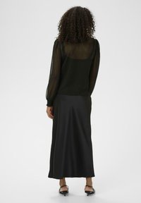 Zwarte, doorzichtige blouse met lange mouwen en een satijnen zwarte maxi rok. Krullend haar, slanker figuur. Zachte textuur met een lichte glans, minimalistisch ontwerp.