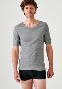 T-shirt grigio a maniche corte con scollatura a V realizzato in tessuto morbido, design fitted e texture liscia; indossato con pantaloni corti neri aderenti.