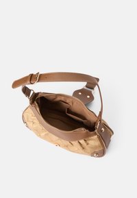 Geantă din material matlasat de culoare bej, cu accente din piele maro, închidere cu fermoar și curea ajustabilă. Interiorul dispune de mai multe buzunare.