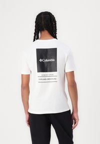 Hvit bomulls t-skjorte med et stort svart boksdesign på baksiden med "Columbia"-logo og tekst "SINCE 1938 PORTLAND, OREGON, USA."