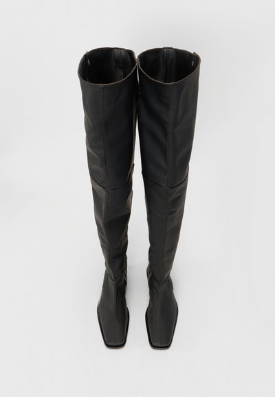 Schwarze knöchelhohe Stiefel aus Leder mit glatter Textur, ausgestattet mit einer spitzen Spitze und einem eleganten, taillierten Design. Sichtbare braune Nähte setzen Akzente.