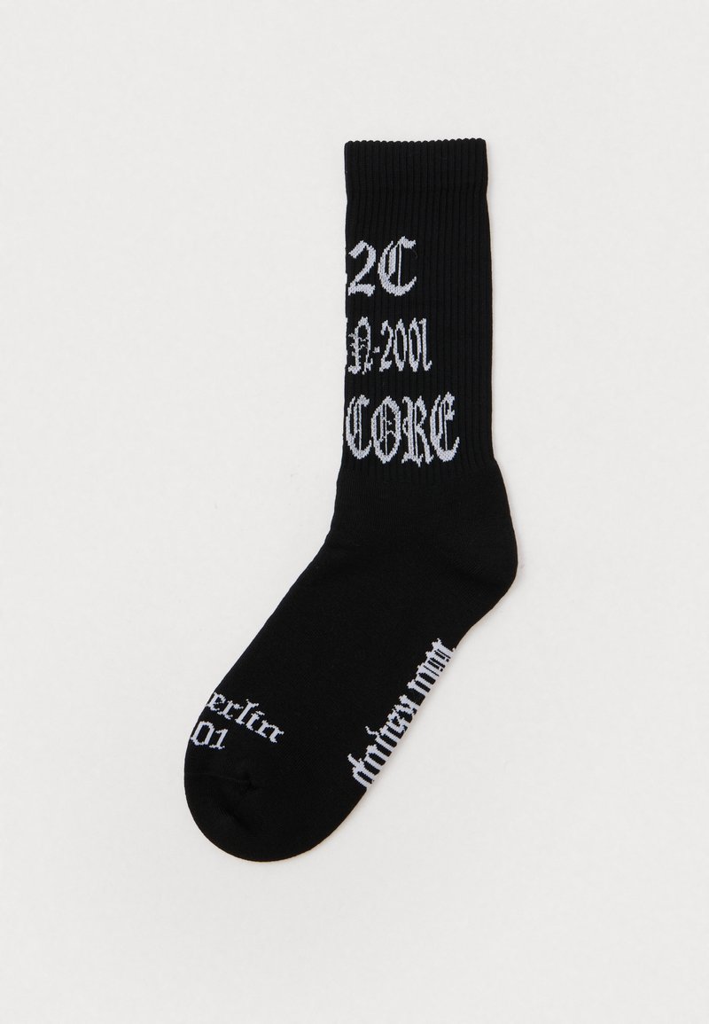 Černé žebrované ponožky s bílým textem, který obsahuje "2C," "A-2001" a "CORE." Design zdůrazňuje gotické písmo.
