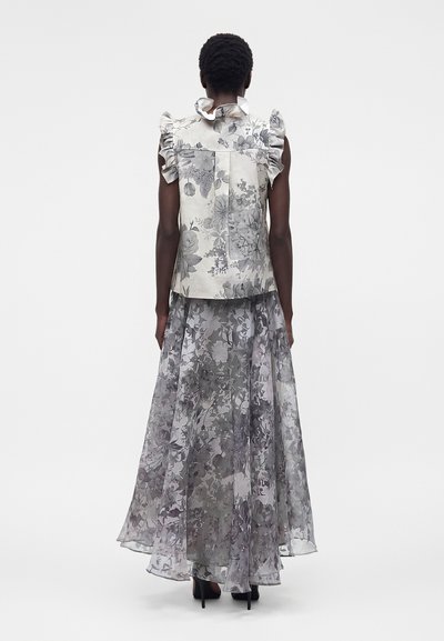 Γυναίκα που φοράει γκρι λουλουδάτο αμάνικο μπλουζάκι με βολάν και ταιριαστό μακρύ, αέρινο, διάφανο φλοράλ φούστα, όρθια με την πλάτη προς το μέρος μας.