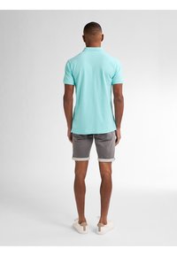 Camisa polo azul claro, pantalones cortos grises con puños enrollados y zapatillas crema. Diseño sencillo con mangas cortas y un cuello clásico.