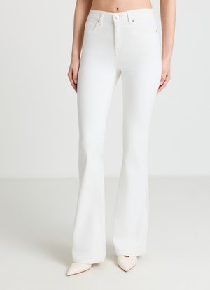 Weiße hoch taillierte, figurbetonte Jeans mit ausgestellten Beinen, getragen mit weißen spitzen Absätzen, gezeigt an einer stehenden Person vor einfarbigem Hintergrund.
