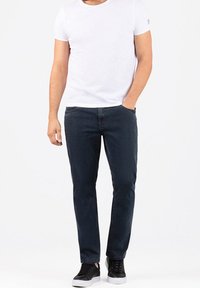 Dunkelblaue Jeans mit Slim-Fit, aus Denim gefertigt. Kombiniert mit einem schlichten weißen T-Shirt und schwarzen Low-Top Sneakern. Einfaches Design, keine sichtbaren Muster.