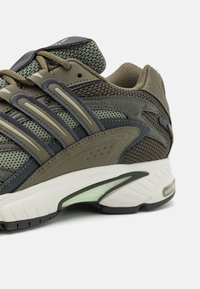 Gröna och gråa träningssneakers med meshpaneler, tre randiga överlägg och en vit mellansula med en genomskinlig accent.