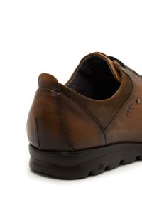 Zapato de cuero marrón con un perfil bajo, tacón redondeado, suela de goma oscura en contraste y detalles de costura sutiles. Marca Fluchos en el lateral.