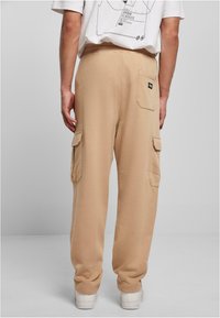 Beiga cargobyxor i sweatpantstil med elastiskt midjeband, sidofickor och en bakficka. Tyget har en mjuk, slät yta.