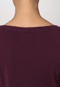 Maglione a maglia color bordeaux con un ampio scollo e una texture morbida, caratterizzato da una vestibilità rilassata e senza decorazioni o motivi visibili.