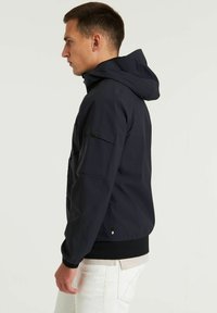Chaqueta con capucha de color azul oscuro hecha de tela suave. Cuenta con un cierre de cremallera en la parte frontal, puños elásticos y un bolsillo lateral con solapa. Diseño de corte ajustado.