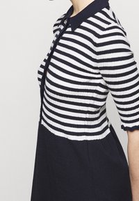 Abito di maglia con un motivo a righe blu navy e bianche, maniche corte e colletto da polo. L'orlo ha un bordo scallop.