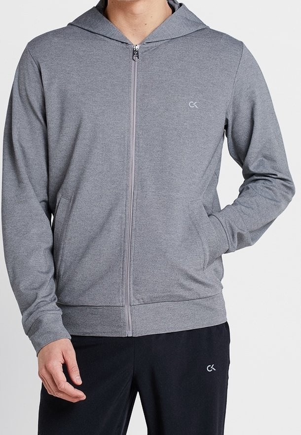 Sudadera gris con cremallera y capucha, hecha de una tela suave. Presenta bolsillos laterales y un logo en el pecho izquierdo. Diseño sencillo con puños acanalados.