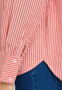 Red and white striped long-sleeve shirt featuring a buttoned cuff, rounded hem, and a relaxed fit. Visible lightweight fabric texture.