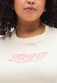 Φούτερ εκρού χρώματος με κόκκινο λογότυπο που γράφει "TOMMY HILFIGER, CO.", με ριμπ γιακά και κοντά μανίκια.