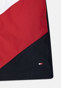 Tkanina v červené a černé barvě s hladkým povrchem; má šití detail a malé logo značky na lemu.