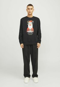 Sort sweatshirt med et farverigt Santa-motiv, rund halsudskæring og ribbede manchetter. Sammen med løstsiddende sorte bukser og hvide sneakers.