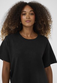 Black knitted sweater with a round neckline and short sleeves. The fabric appears soft and textured, featuring a relaxed fit design.
