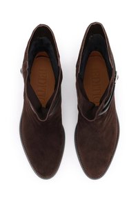 Barna velúr bokacsizmák hegyes orrával, minimalista dizájnnal, látható varrással és diszkrét fekete pánttal a bokán.