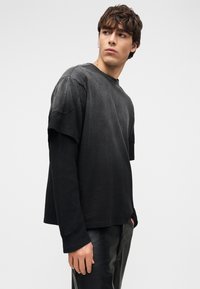 Μαύρο μπλουζάκι με στρώσεις και υφή, με μακρυμάνικο υπόστρωμα. Χαλαρή εφαρμογή, στρογγυλή λαιμόκοψη και ελαφρώς φαρδιά κοντά μανίκια. Μαλακό ύφασμα.